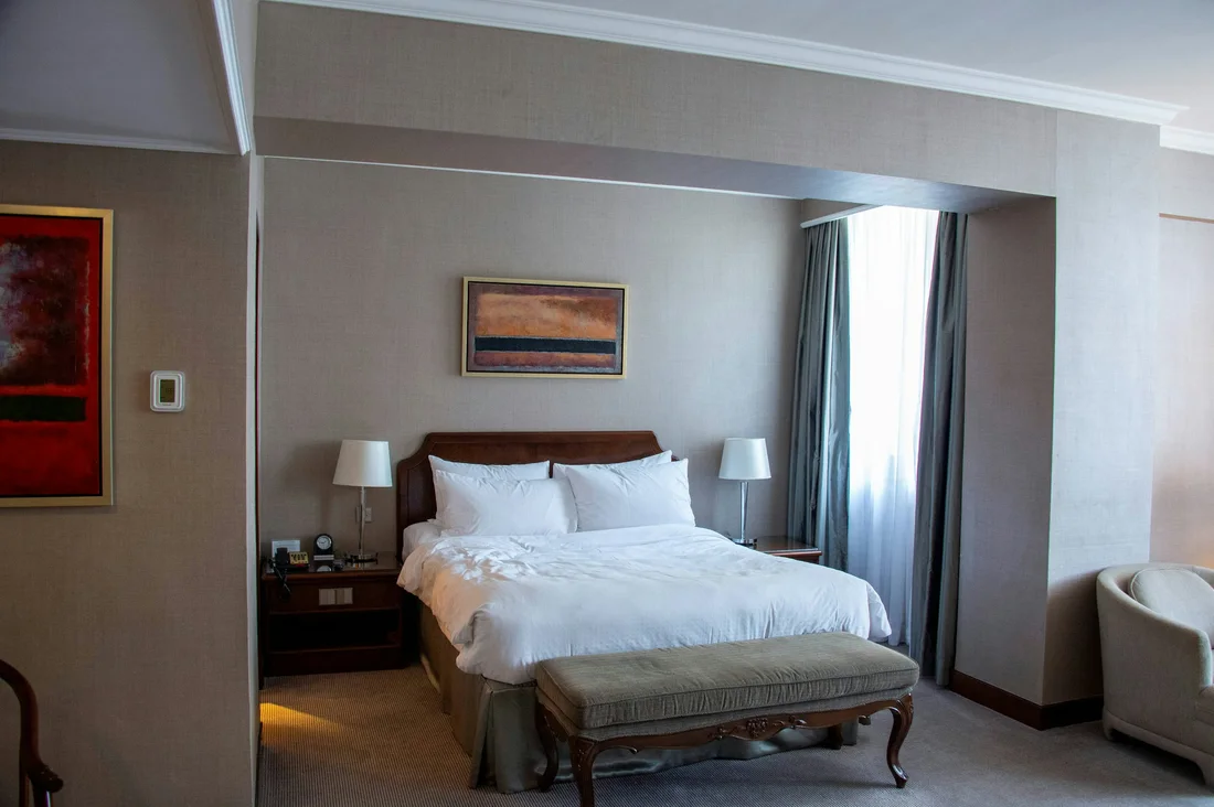 Finished hotel bedroom with bed, bedside furniture, lounge chair and bench