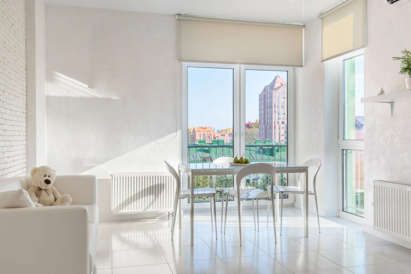 Green upholstered dining chairs around a pale table beside large apartment windows